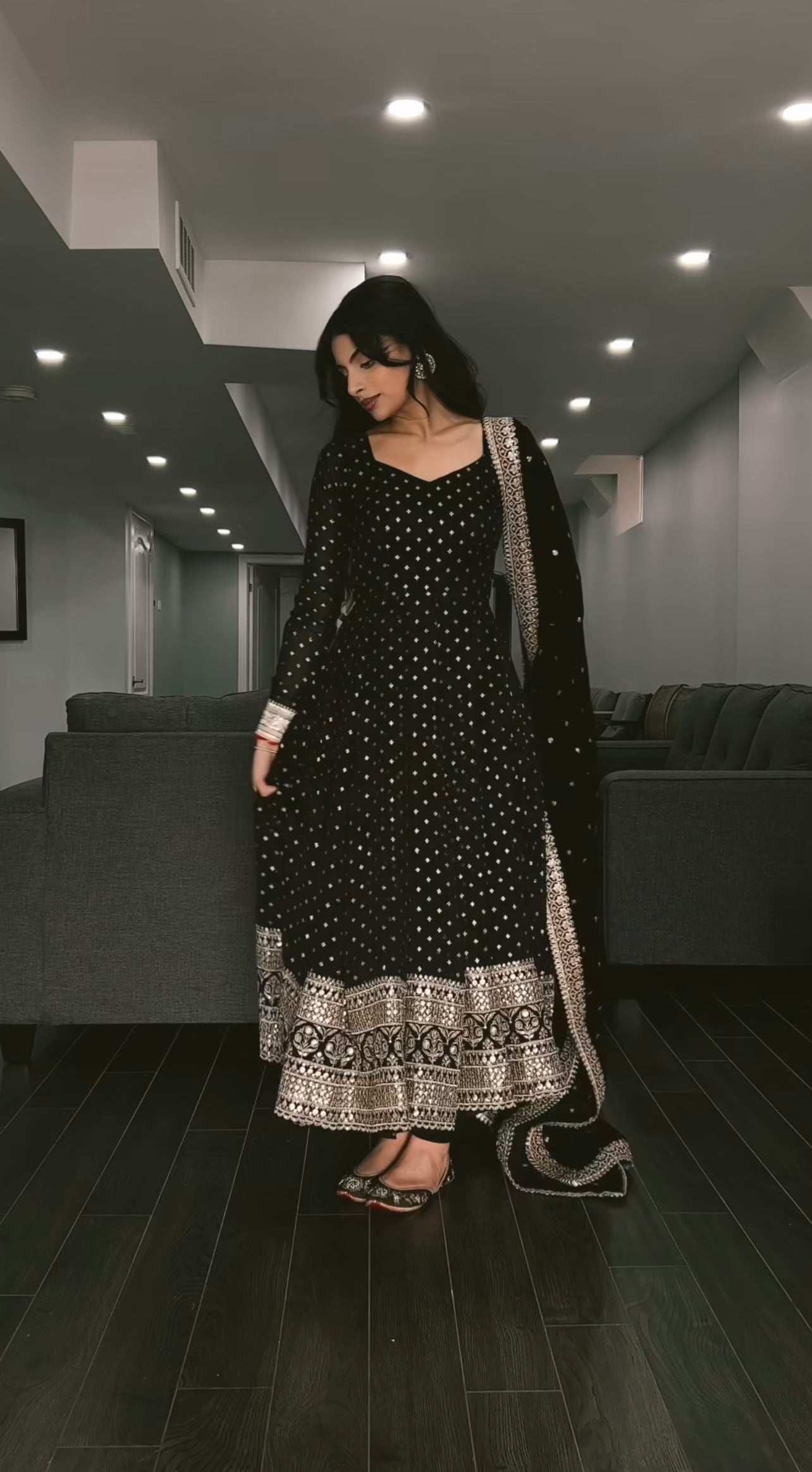 Woman in a black and white traditional outfit standing in a modern interior setting.
