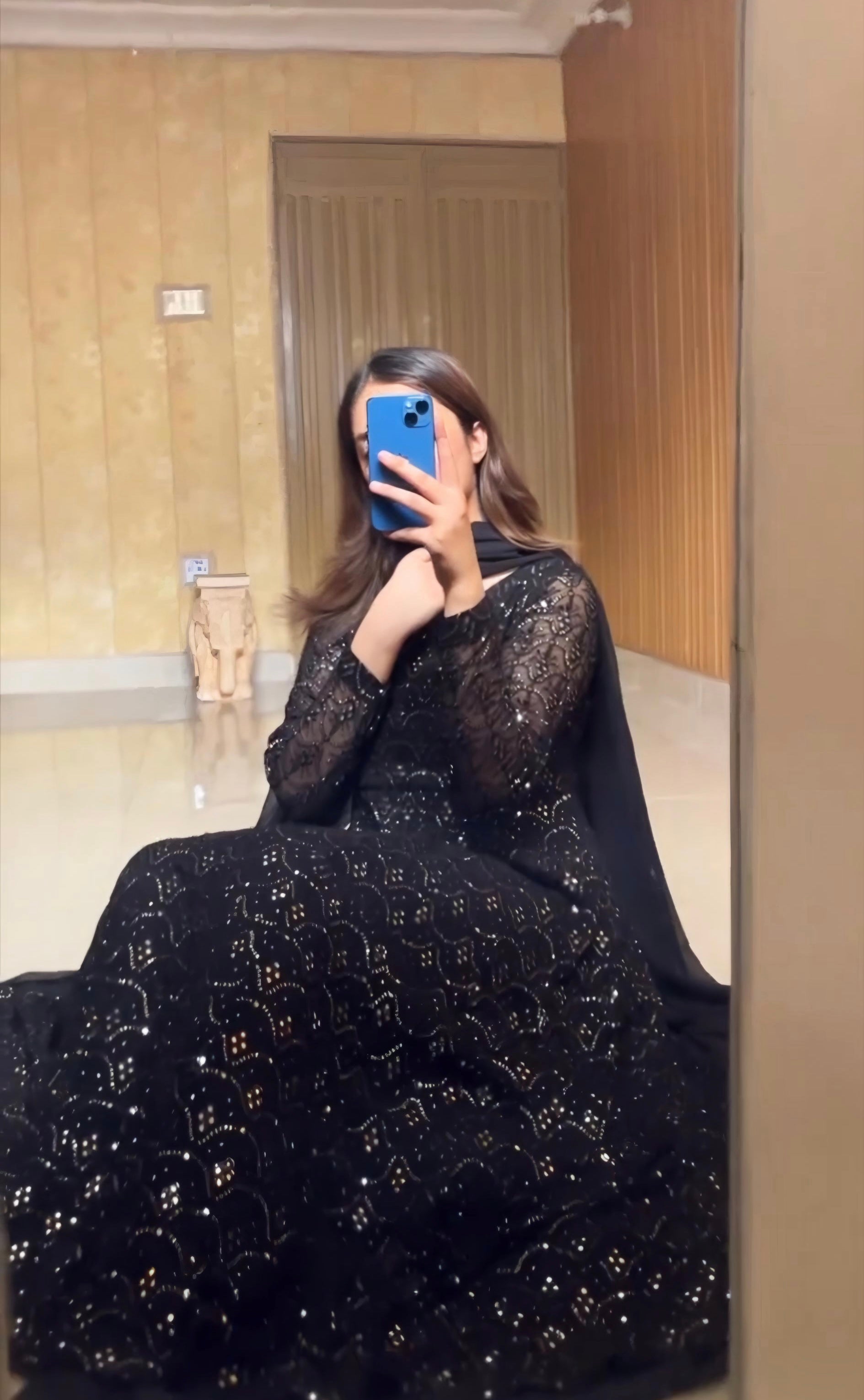 Person wearing a black dress with gold embroidery taking a mirror selfie.