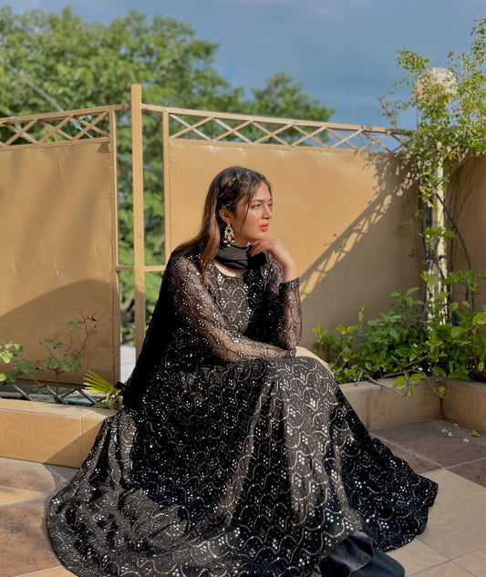 Woman in a black dress sitting outdoors with greenery in the background