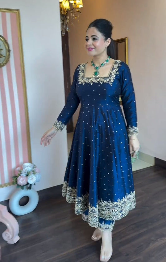 Woman in a blue traditional outfit with white patterns standing indoors.