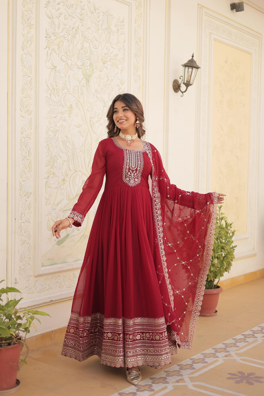 Woman in a red traditional outfit with white embroidery standing in a decorated room.