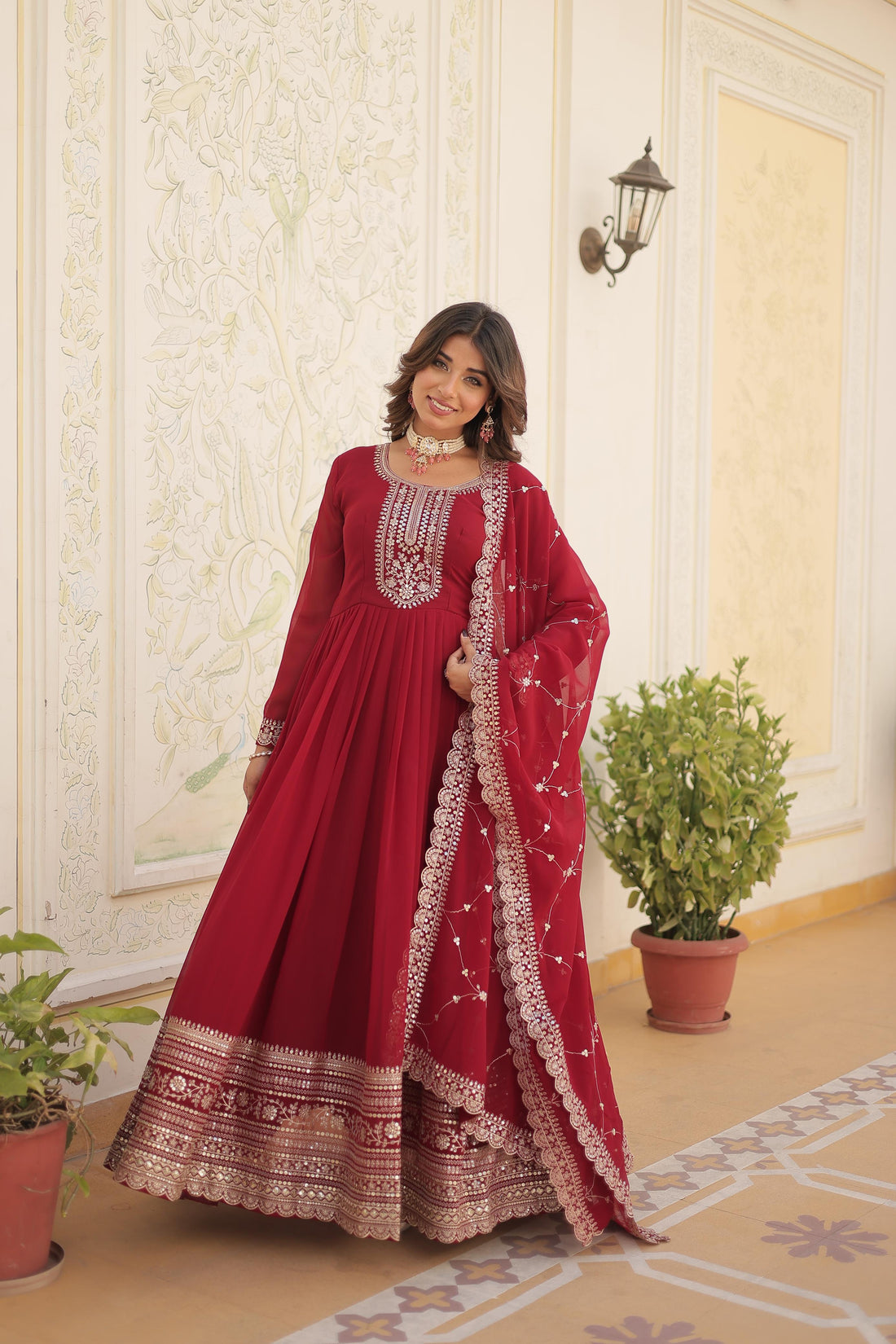 Woman in a red traditional outfit with intricate patterns standing in an elegant room.