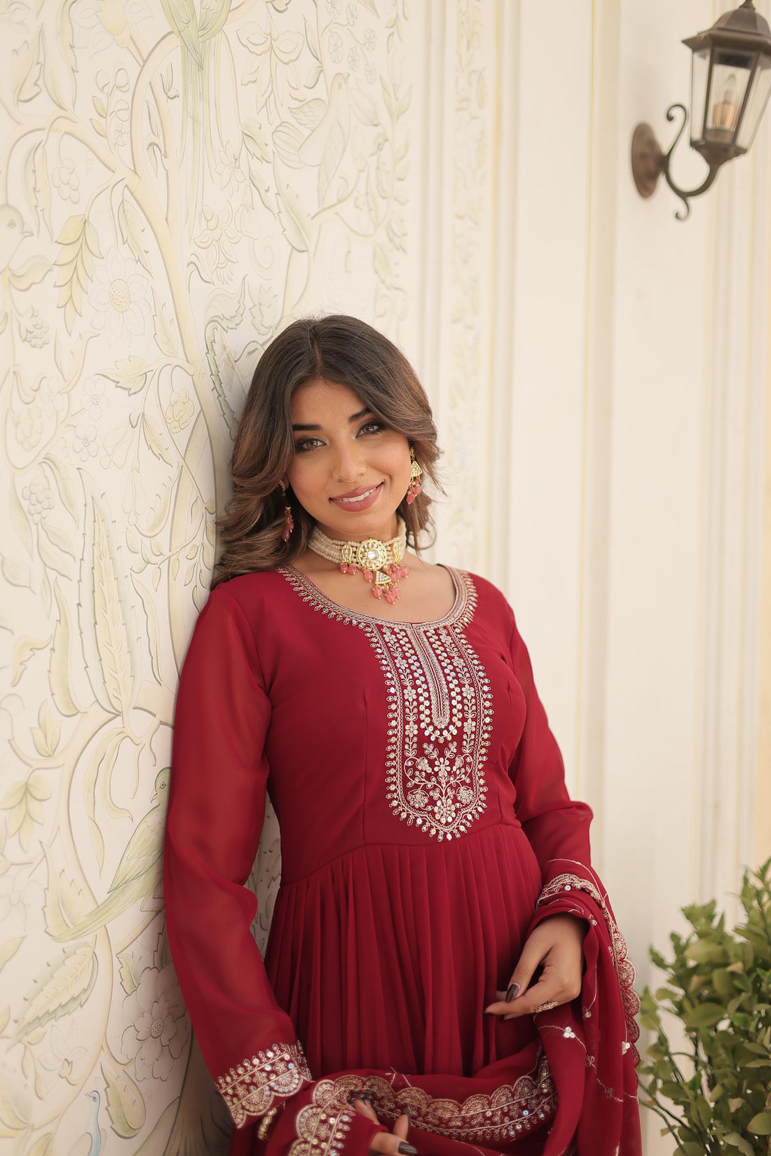 Woman wearing a red embroidered dress against a decorative wall.