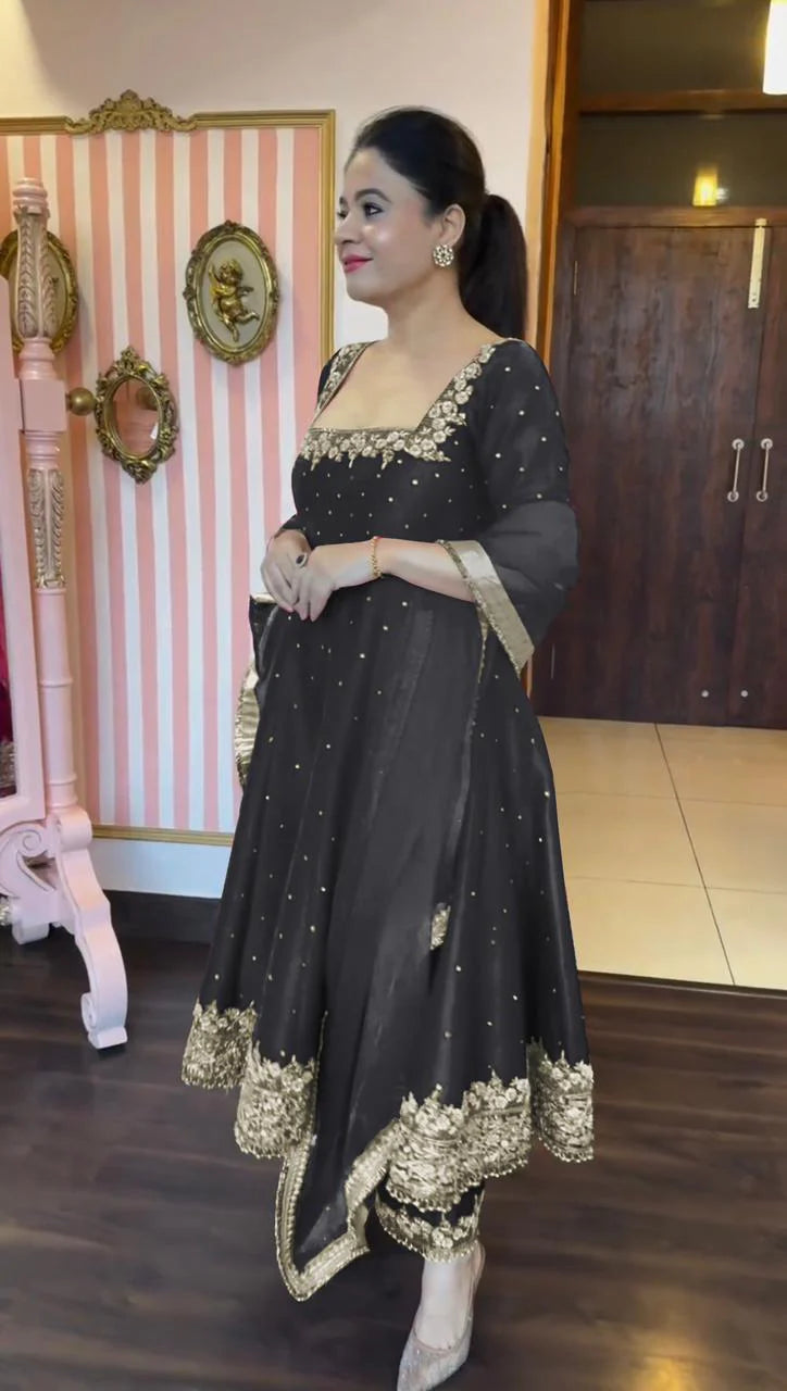 Woman in a black and gold traditional outfit standing indoors.