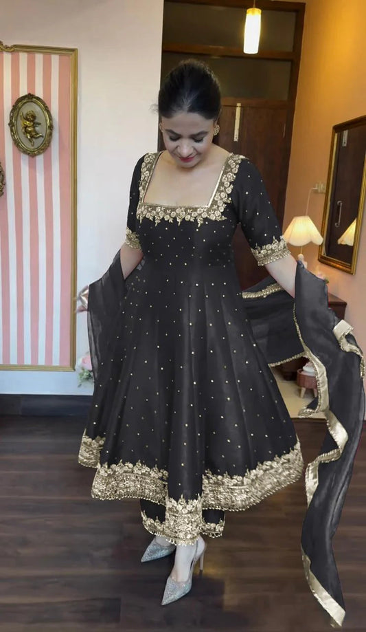 Woman wearing a black traditional outfit with gold embroidery in a room.