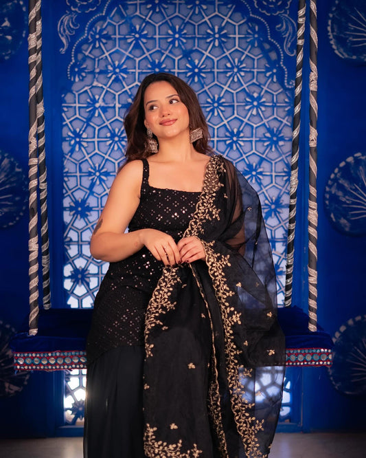 Woman in a black and gold traditional outfit against a blue decorative wall.