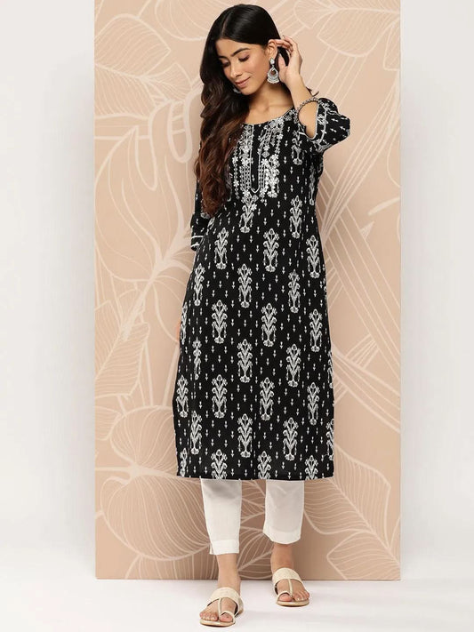 Woman wearing a black and white patterned kurta with white pants against a beige wall.