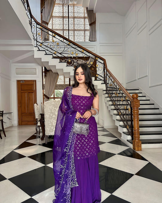 Woman in a purple saree standing in a stylishly decorated interior setting with a staircase.