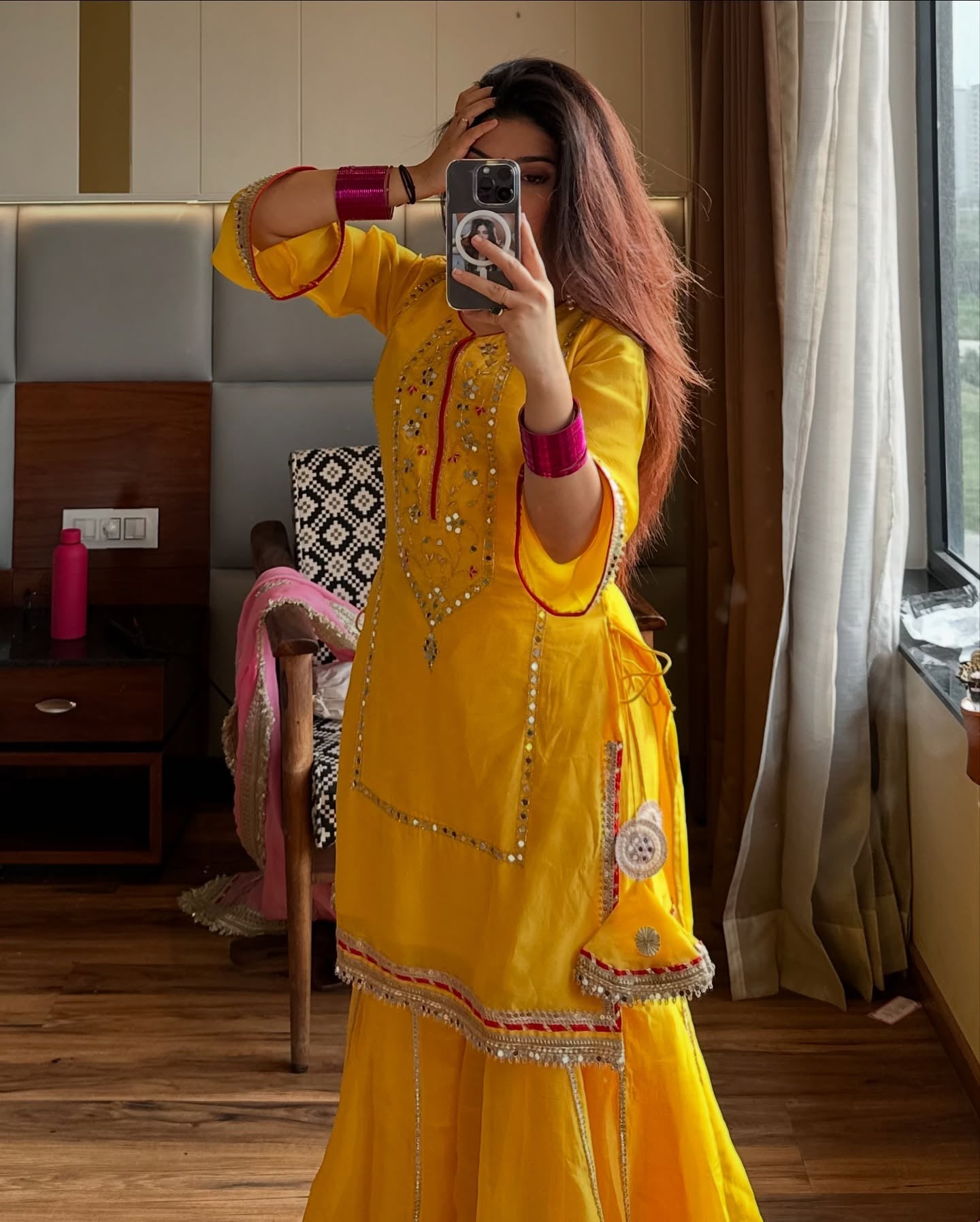 Woman taking a mirror selfie wearing a yellow traditional outfit in a room.