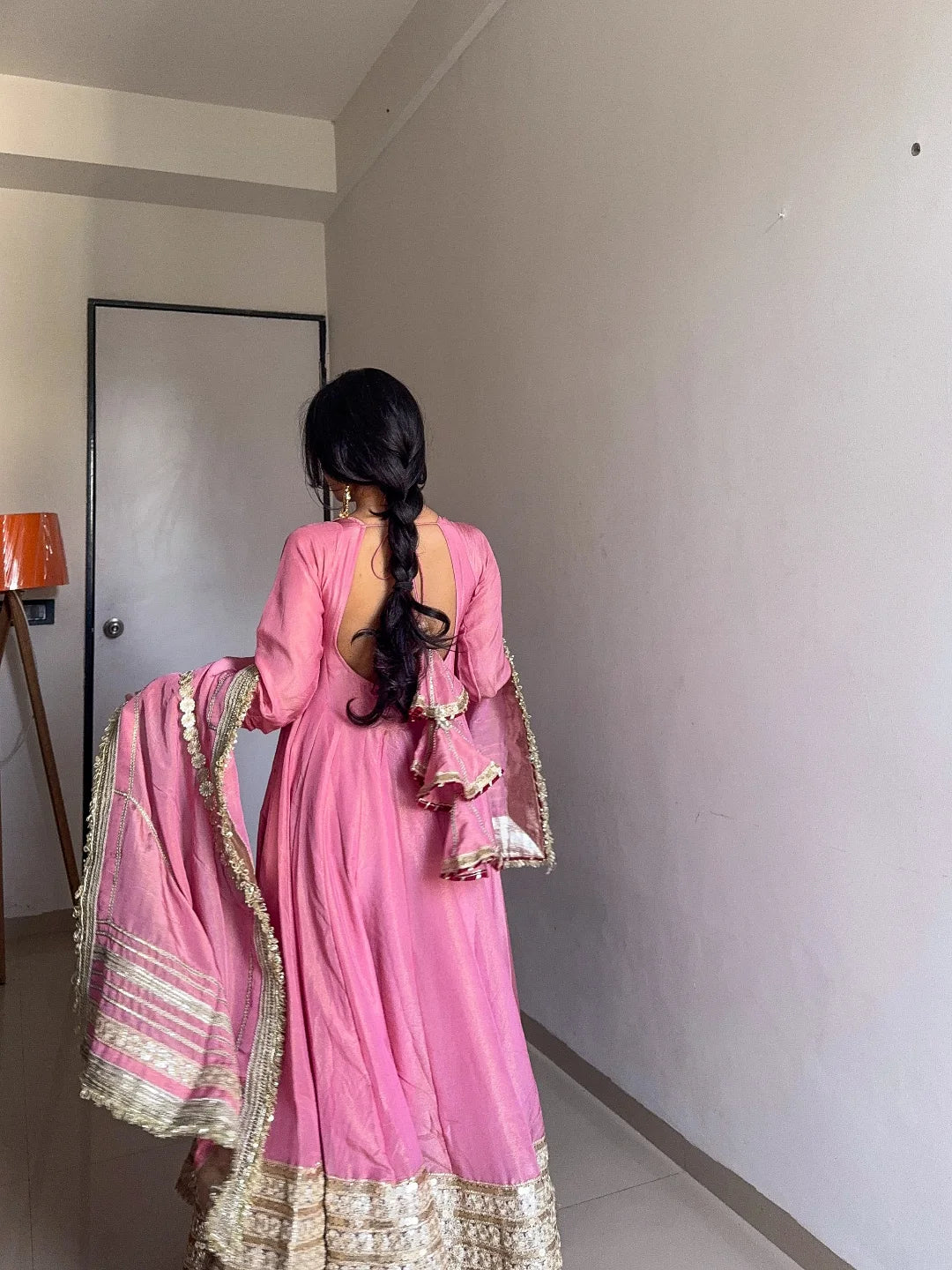 Woman in a pink traditional outfit with gold details standing in a room.