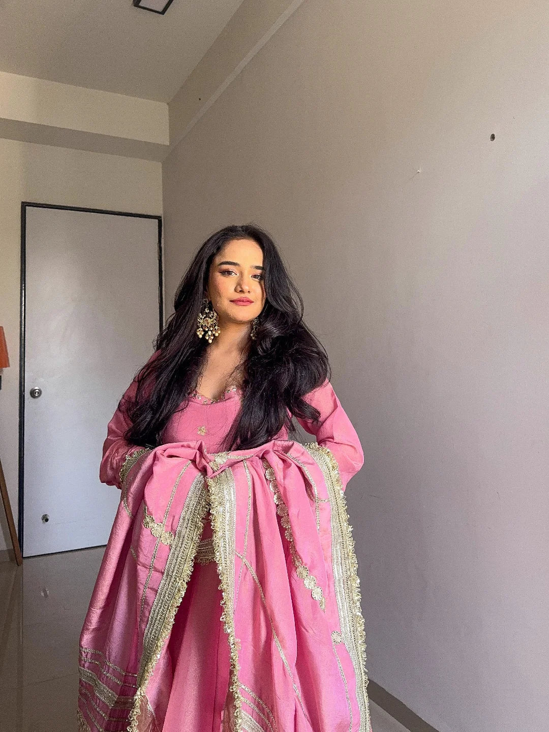 Woman in a pink traditional outfit standing in a room with a neutral background