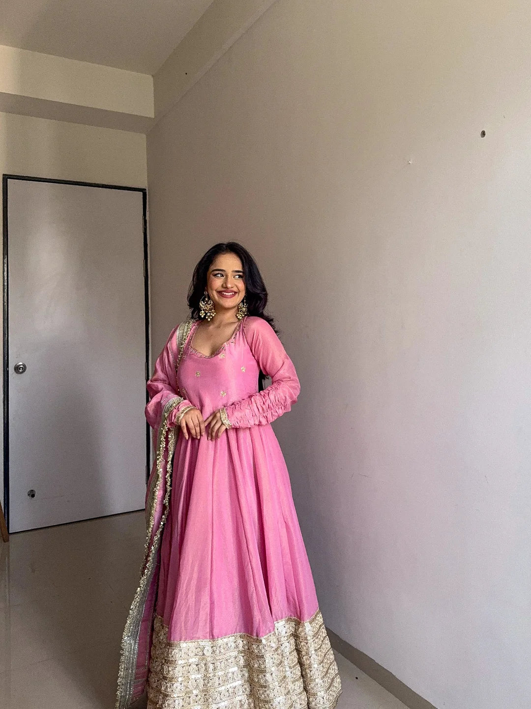 Woman in a pink traditional outfit standing in a room with a white wall and door.