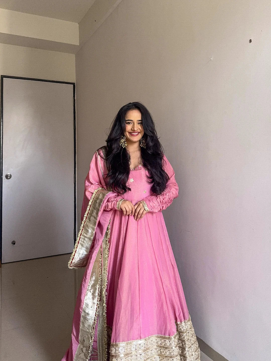 Woman in a pink traditional outfit standing against a plain wall.