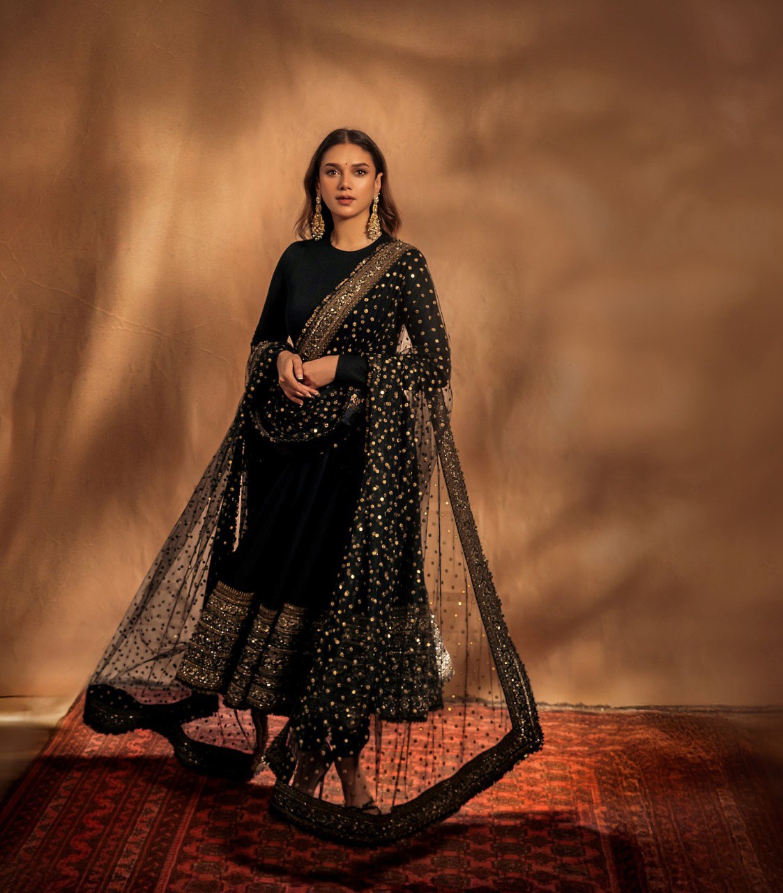 Woman in a black and gold traditional outfit with a draped fabric against a warm-toned background