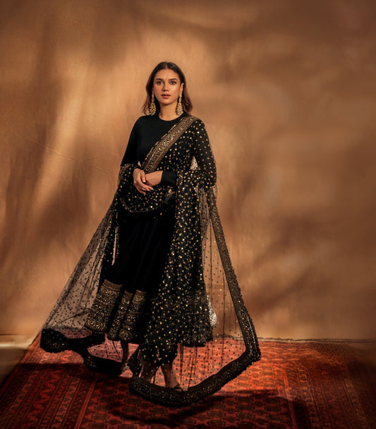 Woman in a black and gold traditional outfit with a draped fabric against a warm-toned background