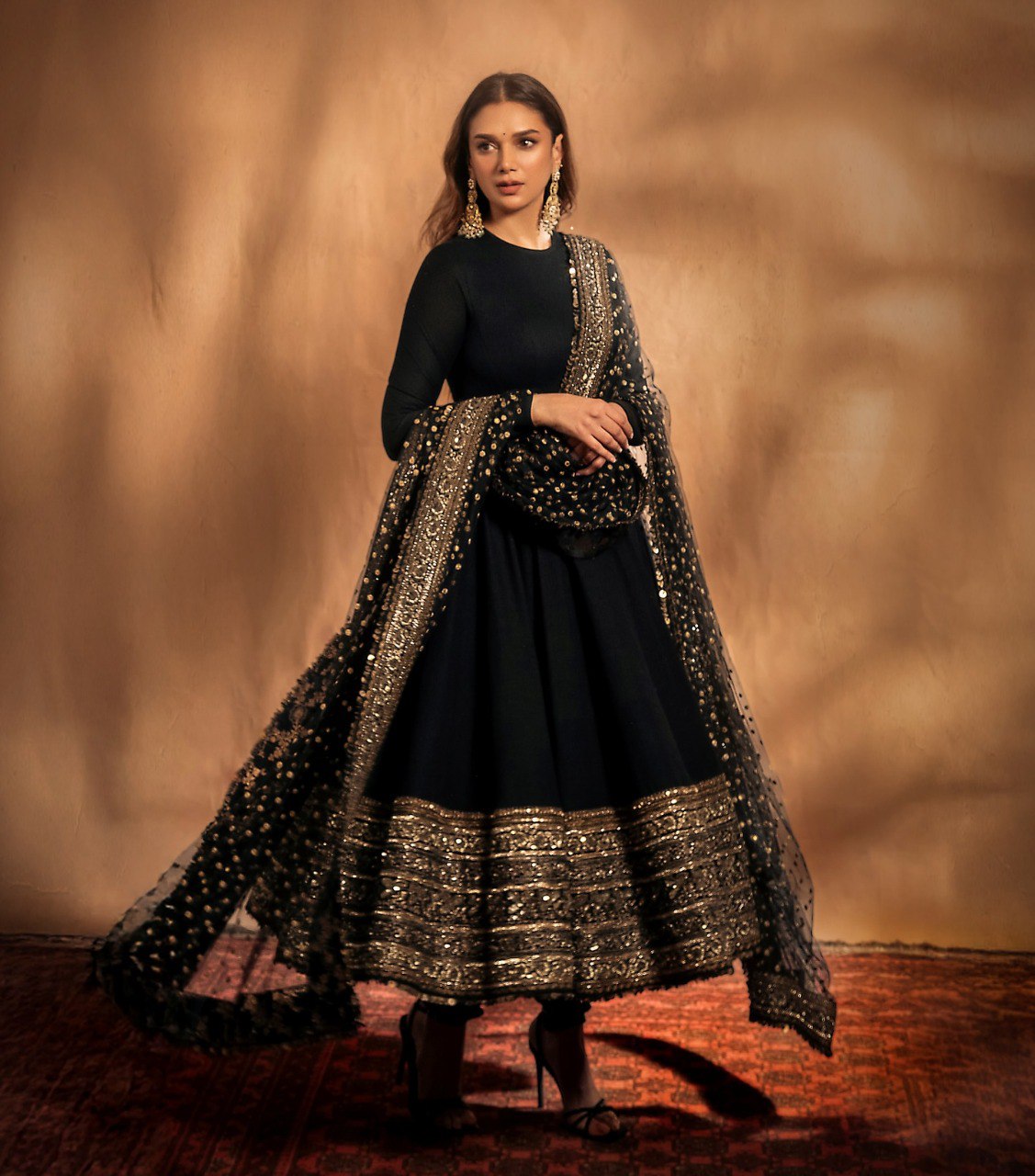 Woman wearing a black traditional outfit with gold embroidery against a warm-toned background