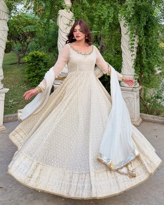 Woman in a white traditional outfit with gold details in an outdoor setting.