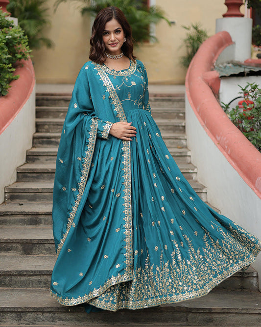 Woman in a teal traditional outfit with gold embroidery standing on steps outdoors.